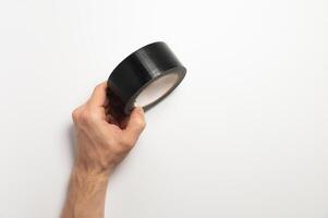 A roll of black reinforced adhesive tape, for sealing joints of roofing materials, when installing the roof, lying, on a white background in a man hand photo