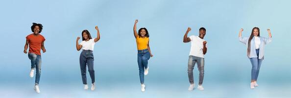 Smiling black young people jumping, making success sign, celebrating victory, enjoy spare time, have fun, isolated on blue studio background, panorama. Winners, free time and lifestyle photo
