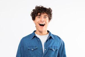 Wow Offer. Excited Curly Guy Looking At Camera Posing With Opened Mouth, Expressing Positivity And Amazement Standing Over White Background In Studio. Portrait Of Surprised Young Man Saying Omg photo