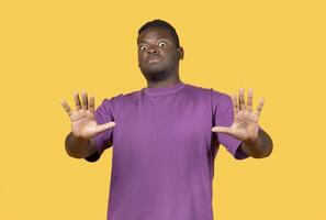Shocked young african american man making stop gesture with hands, pushing camera back standing over yellow background in studio. Disgust, say no and negative emotion, sign of personal space photo