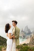 Young couple in love having romantic date, embracing and looking at each other, standing on coastline with beautiful view on ocean shore, vertical shot, copy space photo