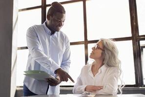 Mentorship At Workplace. African American Businessman Providing Guidance and Support to Employee Woman As Coworker Starting Her New Job, Pointing Finger On Table In Office Indoors photo