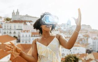 Smiling surprised young african american lady in vr glasses control empty space, abstract lines with hands in city, enjoy game and travel, outdoor. Device online, virtual reality, entertainment photo