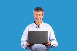 Internet technology and gadgets. Portrait shot of cheerful mature man with laptop advertising online offer, posing holding portable computer and smiling at camera on blue studio background photo