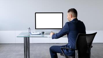 Businessman in formal suit sitting at table in front of computer with blank screen, mockup for business website design. Employee man offering free space for your online advertisement photo