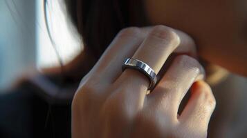 A close-up view of a womans hand with a silver ring on her middle finger. The ring is simple and stylish, with a smooth surface and a slightly rounded edge. The womans skin is soft and pale, and the light reflects off the metal of the ring. photo