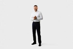 Full body length shot of handsome middle aged man entrepreneur in suit standing posing over light grey studio background and smiling at camera, copy space photo