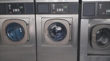 Public Laundry Service. Background With Three Industrial Washing Machines In Laundromat Room Standing In A Row Indoors. Laundrette Equipment And Technology Concept. Panorama photo