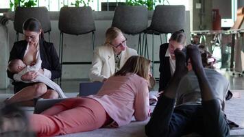 Side view of a group of confident businesswomen in business clothes sitting on a soft carpet in the office and communicating with each other while their colleague a brunette girl in business clothes video