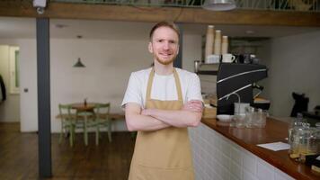 Portrait of a happy blond guy waiter with a beard who crosses his arms on his chest and poses in a cafe video