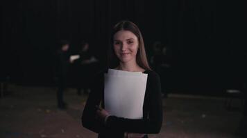 Portrait of a confident young girl actor in a black suit who crosses her arms on her chest while holding play script papers in her hands during a rehearsal in the theater video