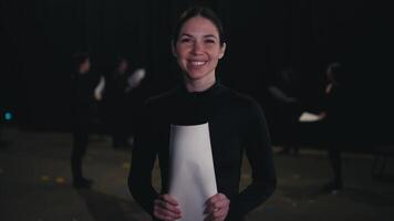 Porträt von ein glücklich und zuversichtlich jung Brünette Mädchen im ein schwarz Darstellerin Kostüm Wer hält Blätter von Skript und Charakter Text im ihr Hände während ihr Vorbereitung zum ein Performance im das Theater video