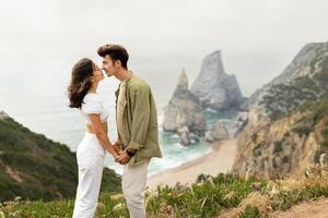 Ocean of affection. Couple in love bonding at coastline, having date on rocks near ocean shore, loving guy and lady enjoying time together, copy space, side view photo