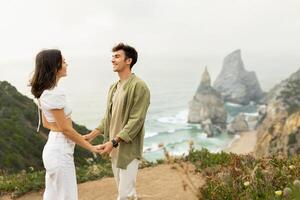 Beachside bonding. Young european couple in love having romantic date, holding hands and looking at each other, standing on coastline with beautiful view, free space photo