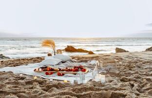 Having picnic with fresh fruits and rose wine on blanket at sandy beach over sea shore at background, free space. Summer season. Vacation time. photo