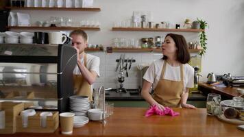 Confident brunette waitress cleans the counter with a pink rag and communicates with a blond guy at the beginning of the working day in a cafe video