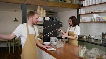A confident brunette barista girl in a yellow apron communicates with a guy waiter and prepares his order while working in a cafe video