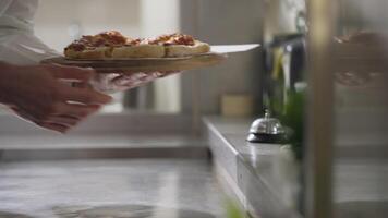 Nearby a waiter in a long white shirt takes ready-made dishes with his own hands and takes them away to take them to the customer. While the cook puts out a new ready-made dish and notifies with a video