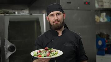 Portrait of a Happy professional male chef in a black uniform with a prepared salad dish in his hands before a presentation in the kitchen in a restaurant video