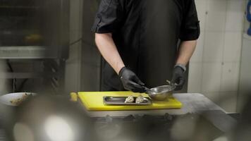 Shot from the side a professional chef in a black uniform and with rubber gloves stuffs small pieces of flour products and prepares a dish in the kitchen in a restaurant video