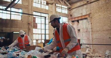 A group of three workers in white uniforms and orange vests recycle garbage and plastic on a conveyor belt at a waste recycling plant. Process of sorting bottles by color at a waste recycling plant video