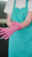 Vertical of a girl in a blue apron a professional cleaner puts on pink rubber gloves before starting cleaning during a In a modern apartment there is a cleaner on call video