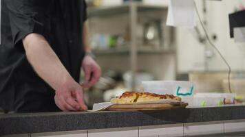 Close up a cook in a black uniform lays out a ready-made dish upon order on the table for distribution in a restaurant from the kitchen. A professional cook lays out the finished dish and notifies you video
