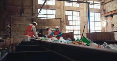 lado Visão do desperdício reciclando plantar trabalhadores dentro especial uniformes deitado Fora e Ordenação plástico garrafas Sediada em seus cor enquanto em pé perto uma comovente transportador cinto às uma grande velho plantar video