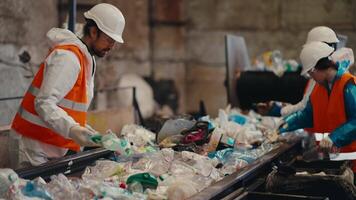 A man in a white uniform an orange vest and a white helmet together with two of his colleagues sorts plastic bottles near a conveyor belt at a large waste recycling and sorting plant video