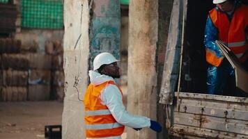 A man with Black skin in a white protective uniform in an orange vest accepts waste paper given to him by a brunette girl from a truck and stores it at the Large Waste Recycling and Sorting Plant video