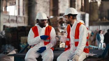 A man with Black skin in a white protective uniform and an orange vest plays rock-paper-scissors with a man and loses to him during his fun and break at work at a waste recycling and sorting plant video