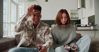 Happy and cheerful man with Black skin color a young brunette with stubble in a cream checkered shirt is very happy about his Victory in a game while sitting with his girlfriend in a sweater on video