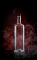 A wet bottle on a beautifully illuminated background. Smoke around a glass bottle. photo