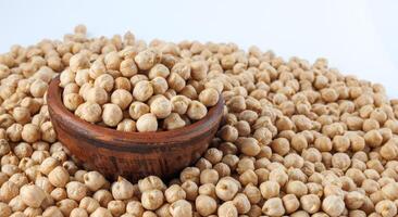 A clay bowl full of chickpeas stands in a pile of scattered chickpeas. Heap of chickpeas on a white background. photo