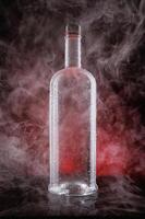 A wet bottle on a beautifully illuminated background. Smoke around a glass bottle. photo