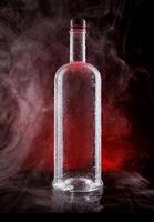 A wet bottle on a beautifully illuminated background. Smoke around a glass bottle. photo