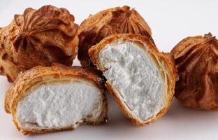 Cut in half and whole porophytroles with white cream on a white background. Eclair with cream. photo