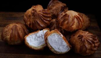 Profiteroles with white custard on a wooden board. Mini eclairs with white cream. photo