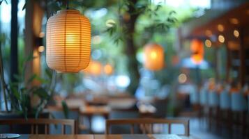 Lanterns create a warm glow in a cozy outdoor cafe setting at dusk, with blurred background foliage and seating. photo