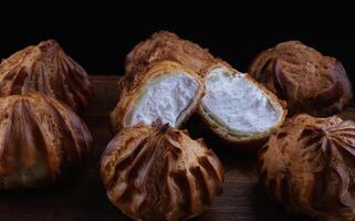 Profiteroles with white custard on a wooden board. Mini eclairs with white cream. photo