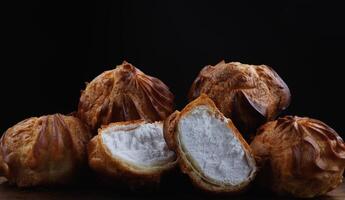 Profiteroles with white custard on a wooden board. Mini eclairs with white cream. photo