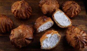 Profiteroles with white custard on a wooden board. Mini eclairs with white cream. photo