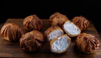 Profiteroles with white custard on a wooden board. Mini eclairs with white cream. photo