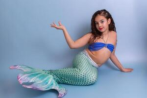 A beautiful elegant girl in a mermaid costume lies on a blue background with her palm raised up. photo