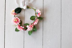 Top view of wreath of textile pink flowers lies on a white wooden table photo