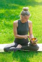 A woman sitting on mat on the green grass in the park in summer, holds a meditation bowl. photo