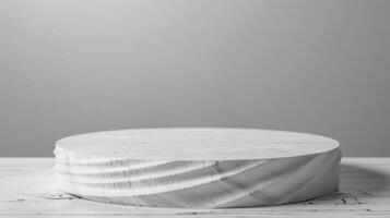 A round wooden platform stands on a white marble surface under soft lighting. The background is plain and gray, creating a minimalist look. photo