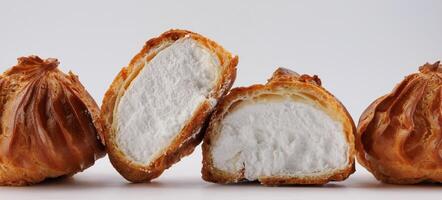 Cut in half and whole porophytroles with white cream on a white background. Eclair with cream. photo