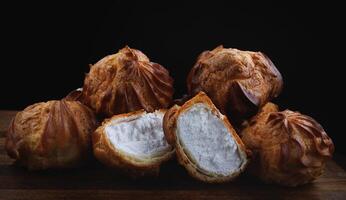 Profiteroles with white custard on a wooden board. Mini eclairs with white cream. photo