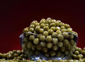 Canned green peas in a glass cup and scattered around it. Beautifully illuminated background. photo
